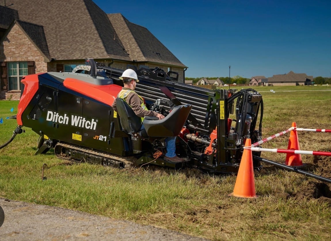 Worker operating a Ditch Witch trenching machine in a residential yard with safety cones nearby